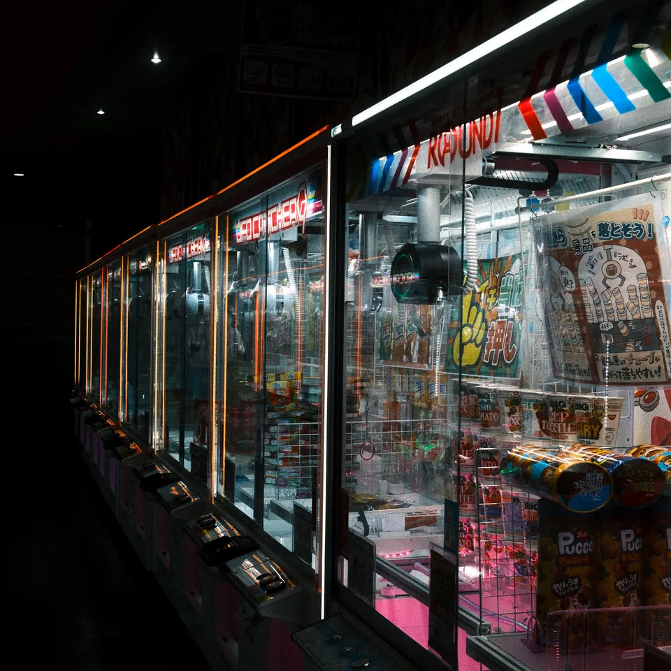 A row of illuminated claw machines filled with snacks in a dark arcade.