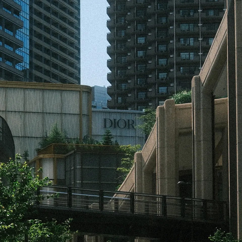 A curving road beneath a pedestrian bridge, surrounded by tall buildings and greenery.